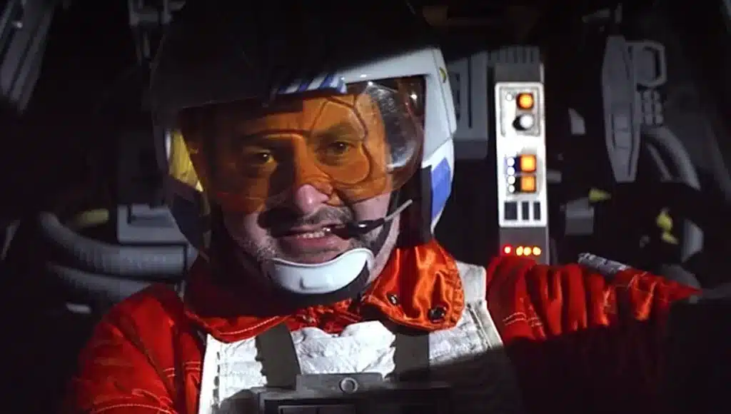 Pilot in spaceship wearing red flight suit and helmet.