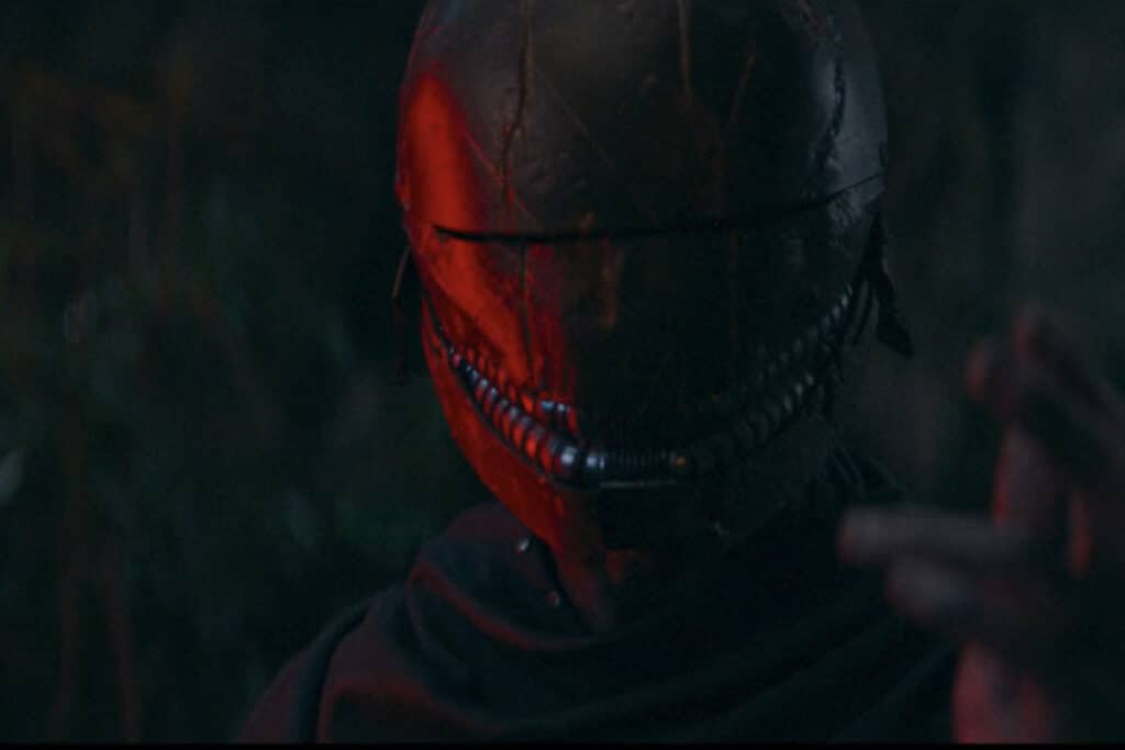 Person in red-lit medieval helmet and black robe