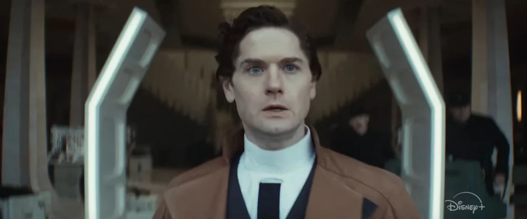 Syril Karn in Andor Season 2, portrayed by Kyle Soller, standing determined in an Imperial facility. His journey from law-abiding officer to manipulated pawn showcases his tragic fall under the Empire's influence.