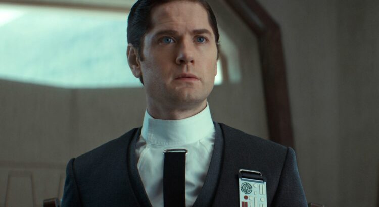 Syril Karn dressed in Imperial attire during a tense moment in Andor. His belief in law and order drives his actions, despite his naive trust in the Empire's ideals of justice.