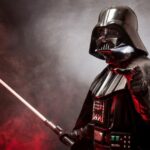 Darth Vader pointing with red lightsaber against smoky red and gray background