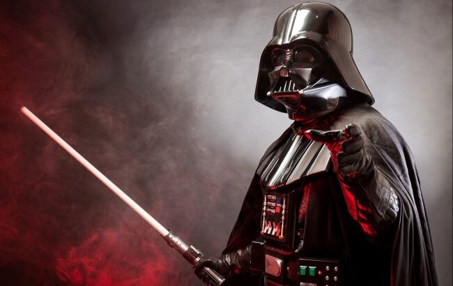 Darth Vader pointing with red lightsaber against smoky red and gray background