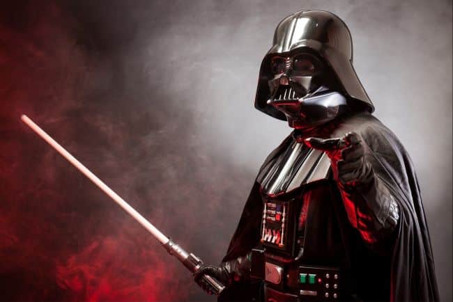 Darth Vader pointing with red lightsaber against smoky red and gray background