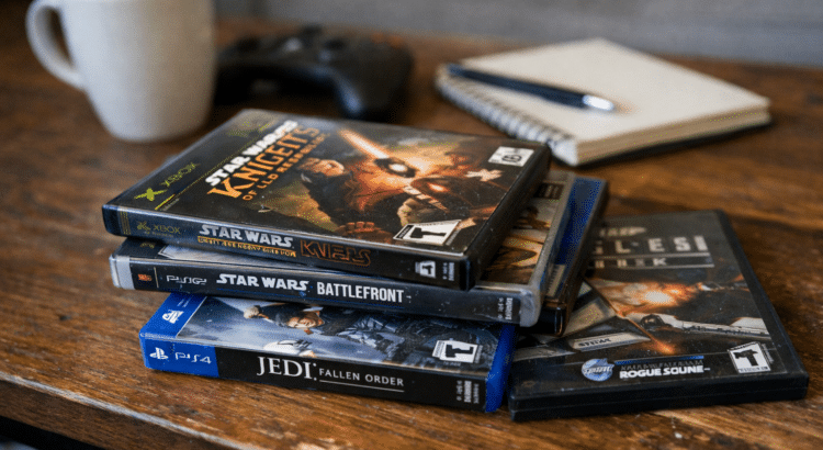 Stack of classic Star Wars video game cases including Knights of the Old Republic, Battlefront II, Jedi Survivor, and The Old Republic on a wooden table