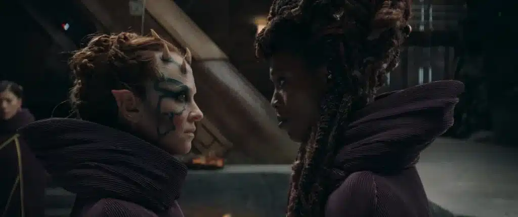Two women in futuristic attire facing off indoors