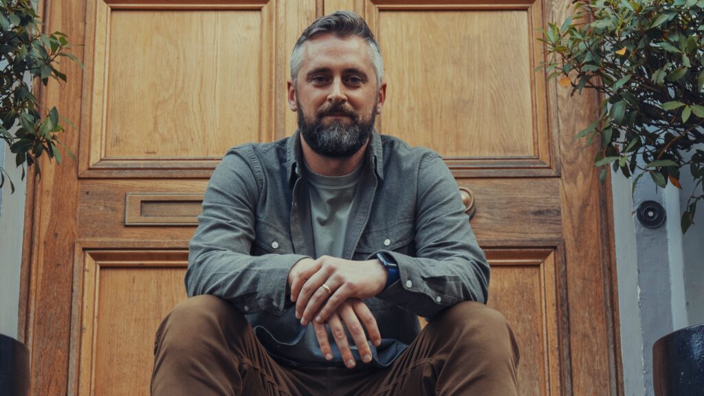 Bearded man sitting on front steps by wooden door